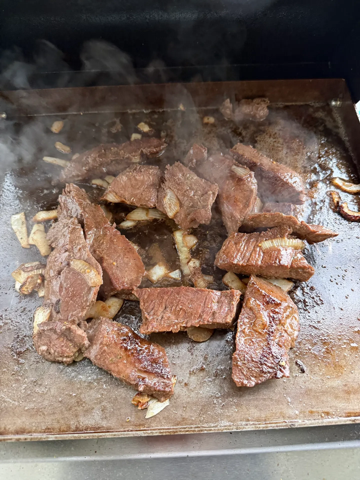 Strips of elk backstrap and onions cooking on a griddle over a pellet grill